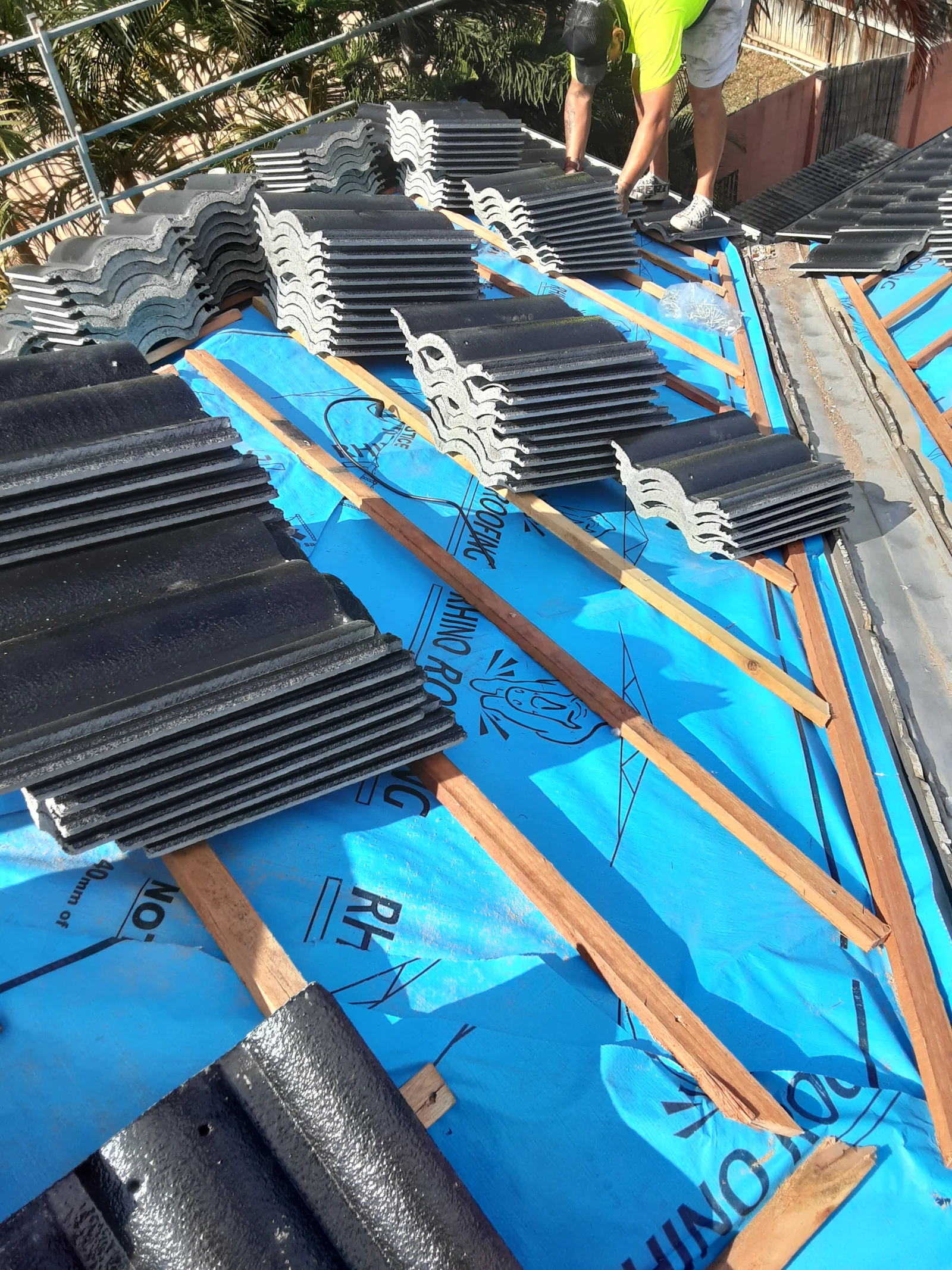 Roof restoration in progress on a Brisbane home showing stacks of black roof tiles on blue sarking before installation