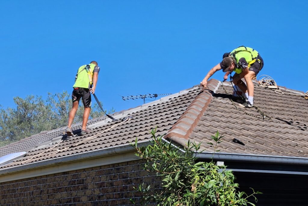 Two Storm Call roofers in harnesses removing damaged ridge capping on a tiled roof in Brisbane