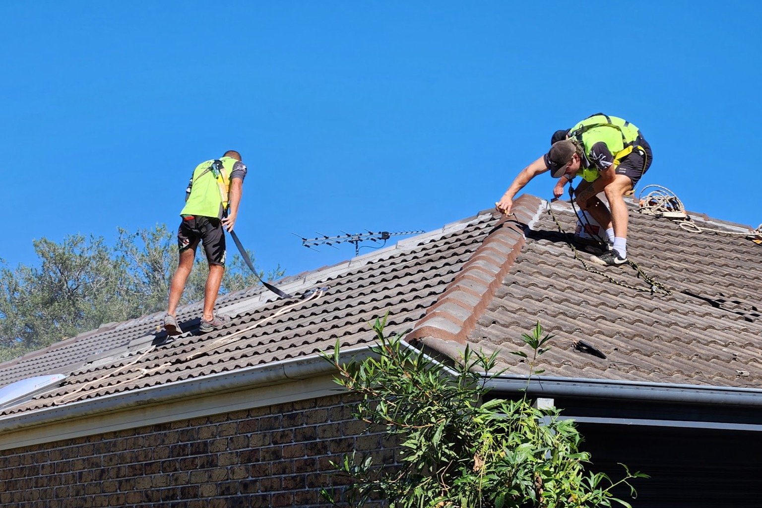 Two Storm Call roofers in harnesses removing damaged ridge capping on a tiled roof in Brisbane